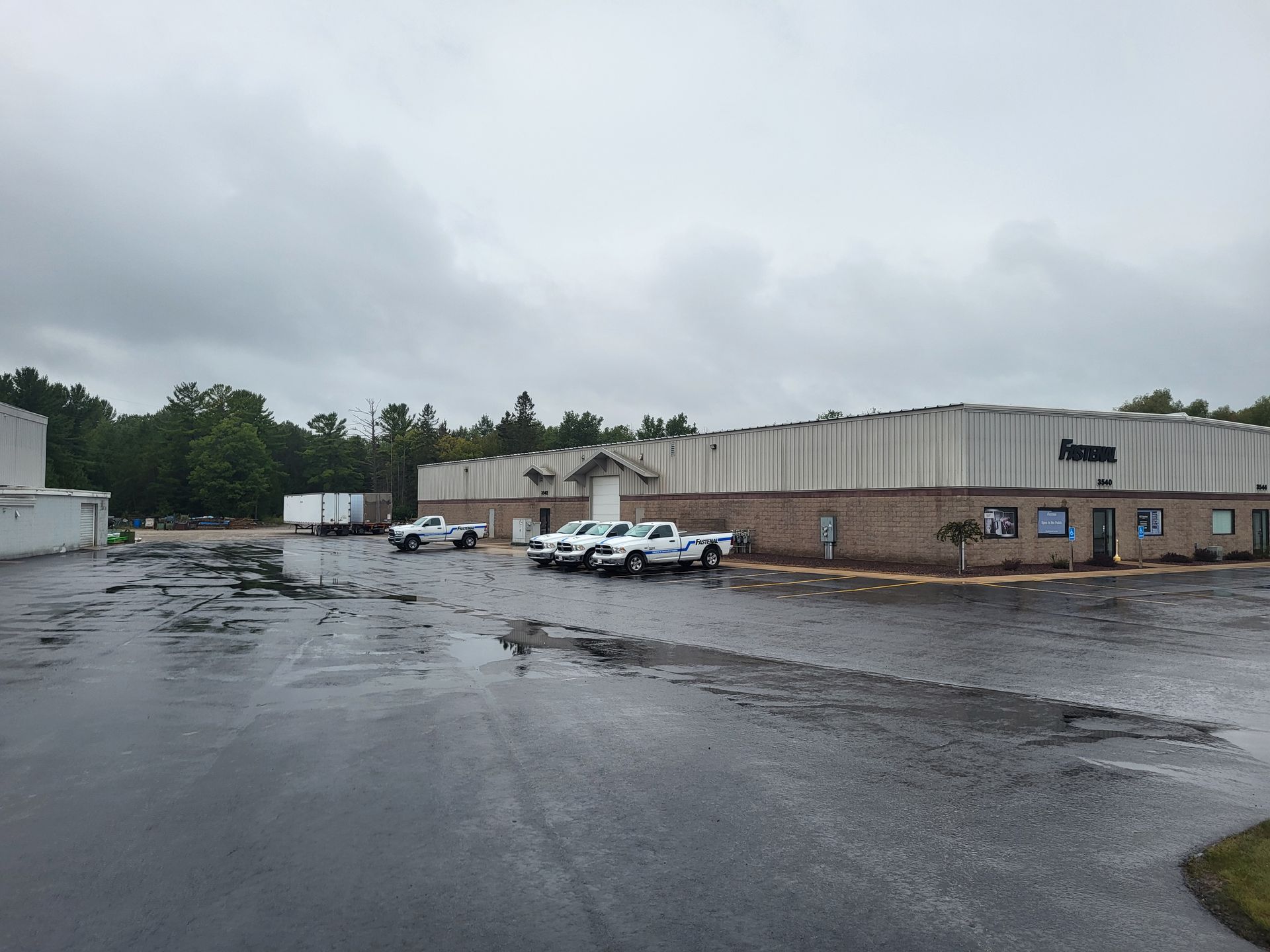 A large building with trucks parked in front of it on a cloudy day. The pavement is freshly sealcoated by Alpena Asphalt Armor LLC