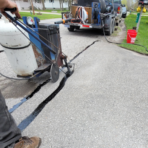 employee of aaalllc using a hot rubber mixture to fill in cracks in the asphalt