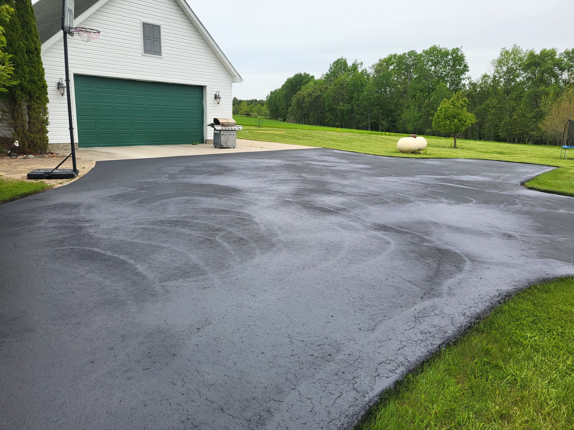 A newly sealcoated driveway with a green garage door and a basketball hoop in front of a house.