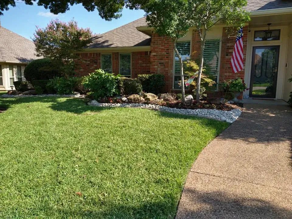 A brick house with a lush green lawn and an american flag in front of it.