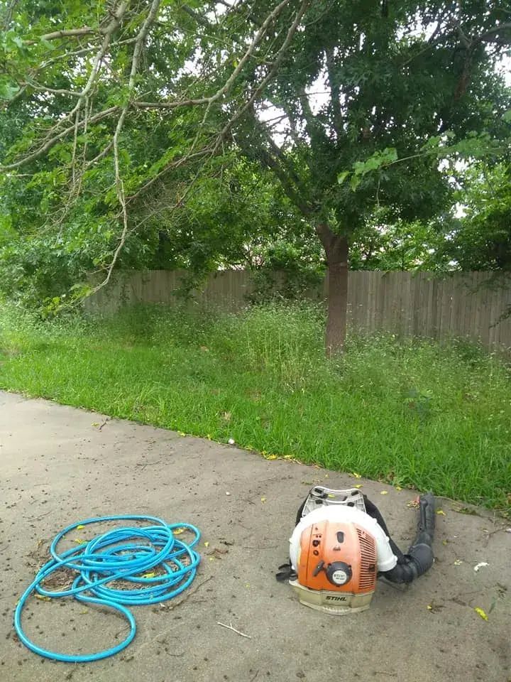 A backpack blower is sitting on the sidewalk next to a hose.