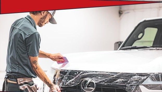 Man applying clear film to the hood of a white truck in a garage, using a squeegee.