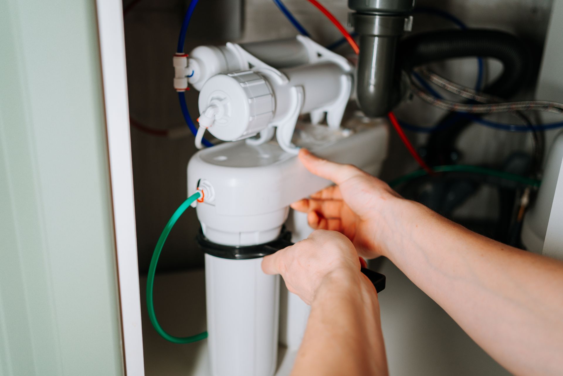 Hands installing a white water filter cartridge under a sink