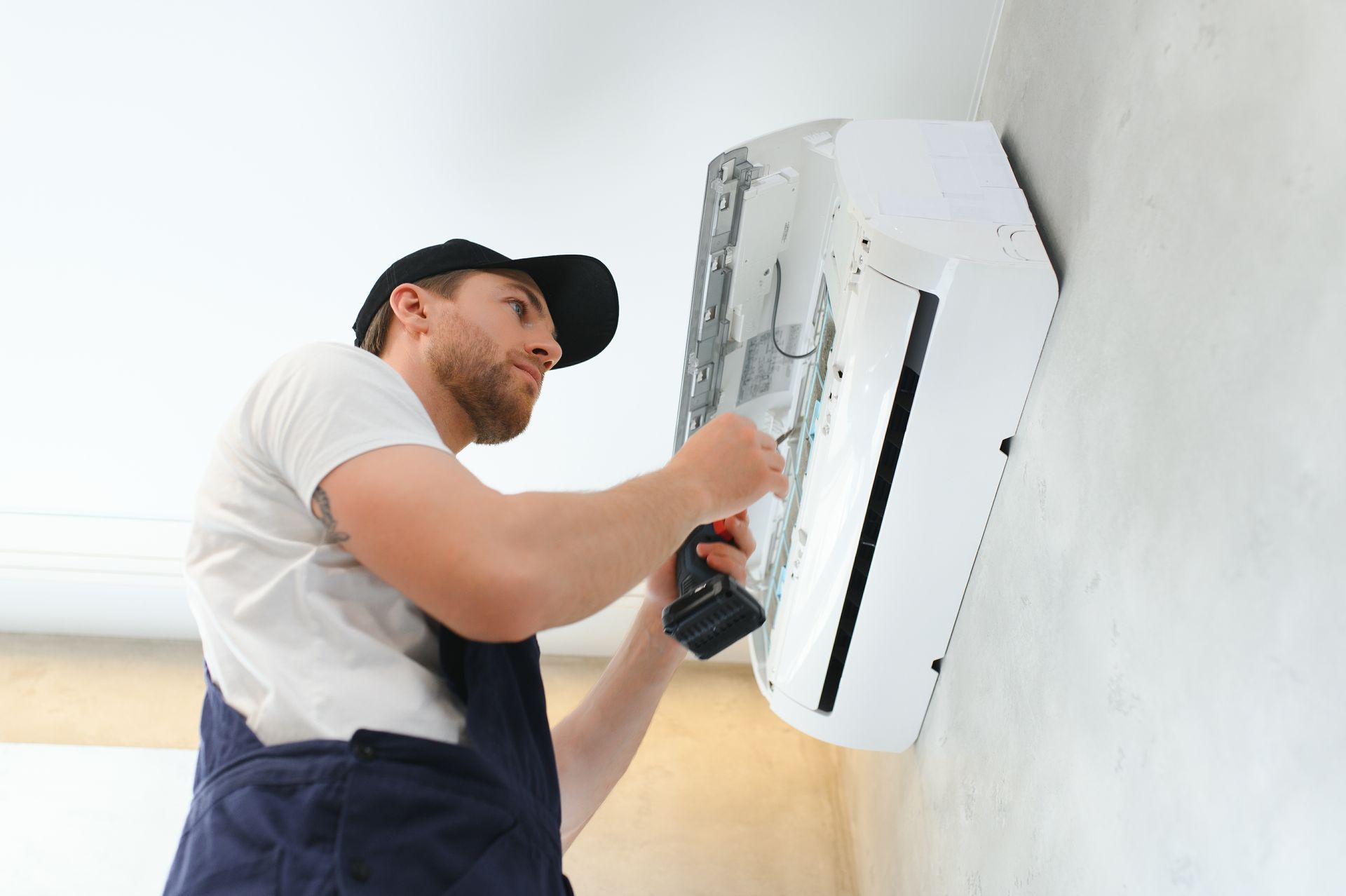 A worker opening and repairing a wall AC unit with a drill during routine maintenance. A worker opening and repairing a wall AC unit with a drill during routine maintenance.