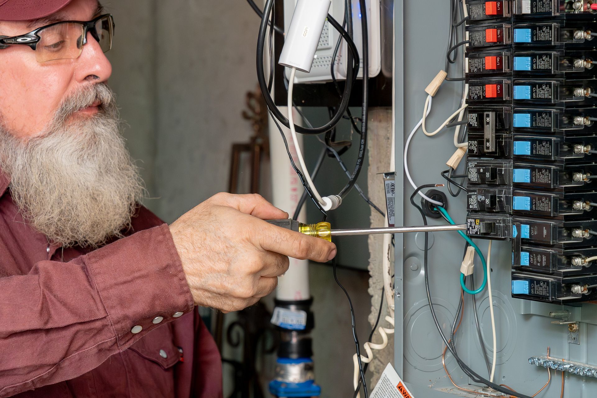 A man with a beard is working on an electrical box with a screwdriver.