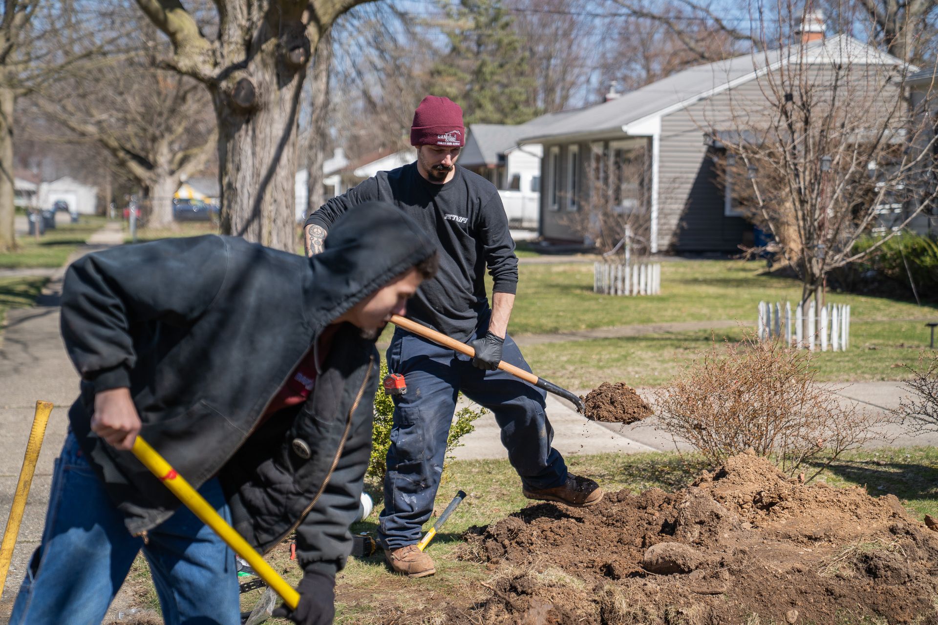 Two men are digging in the dirt in front of a house.