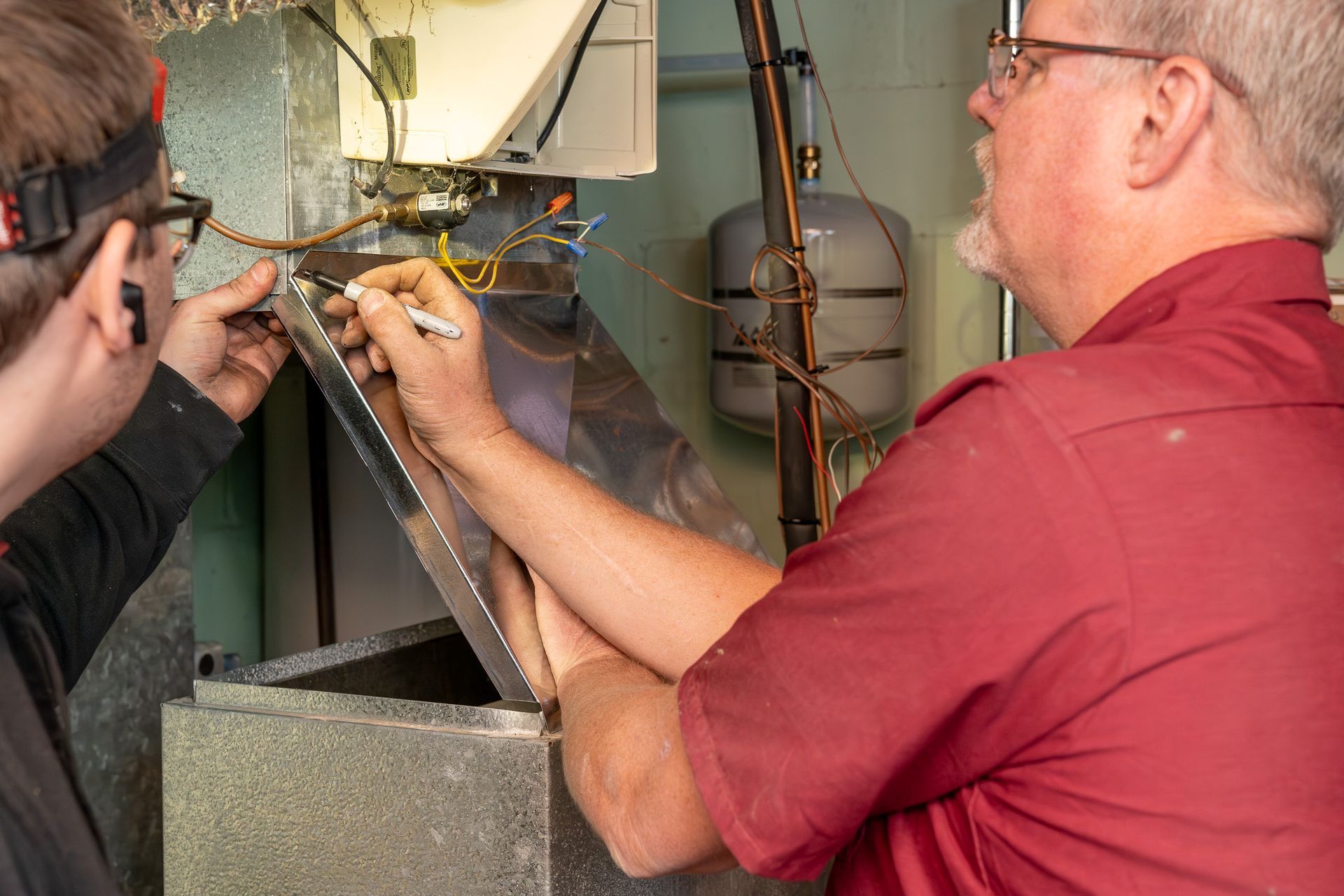 Two men are working on a heater in a garage.