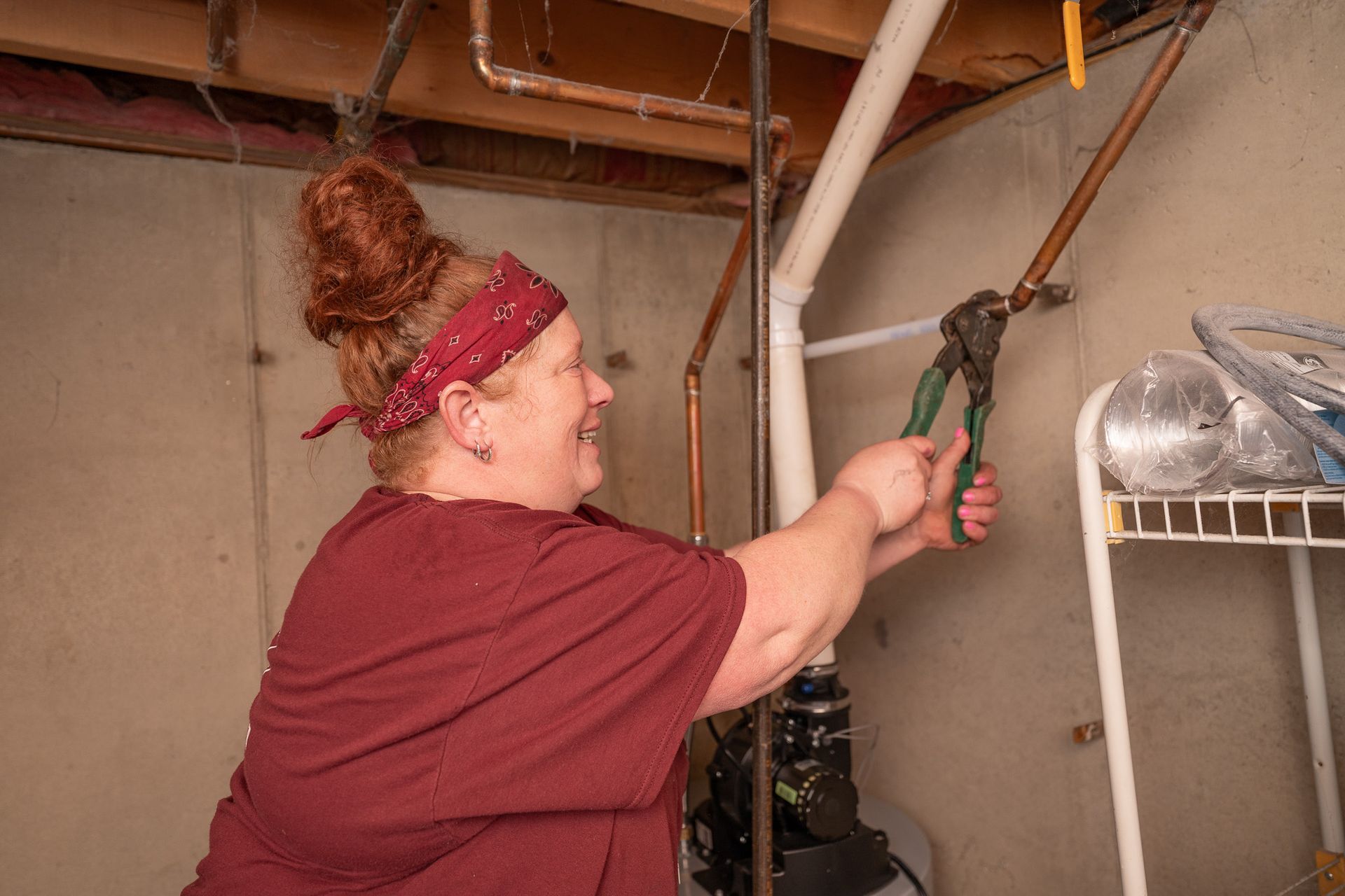 A woman is working on a pipe in a basement.