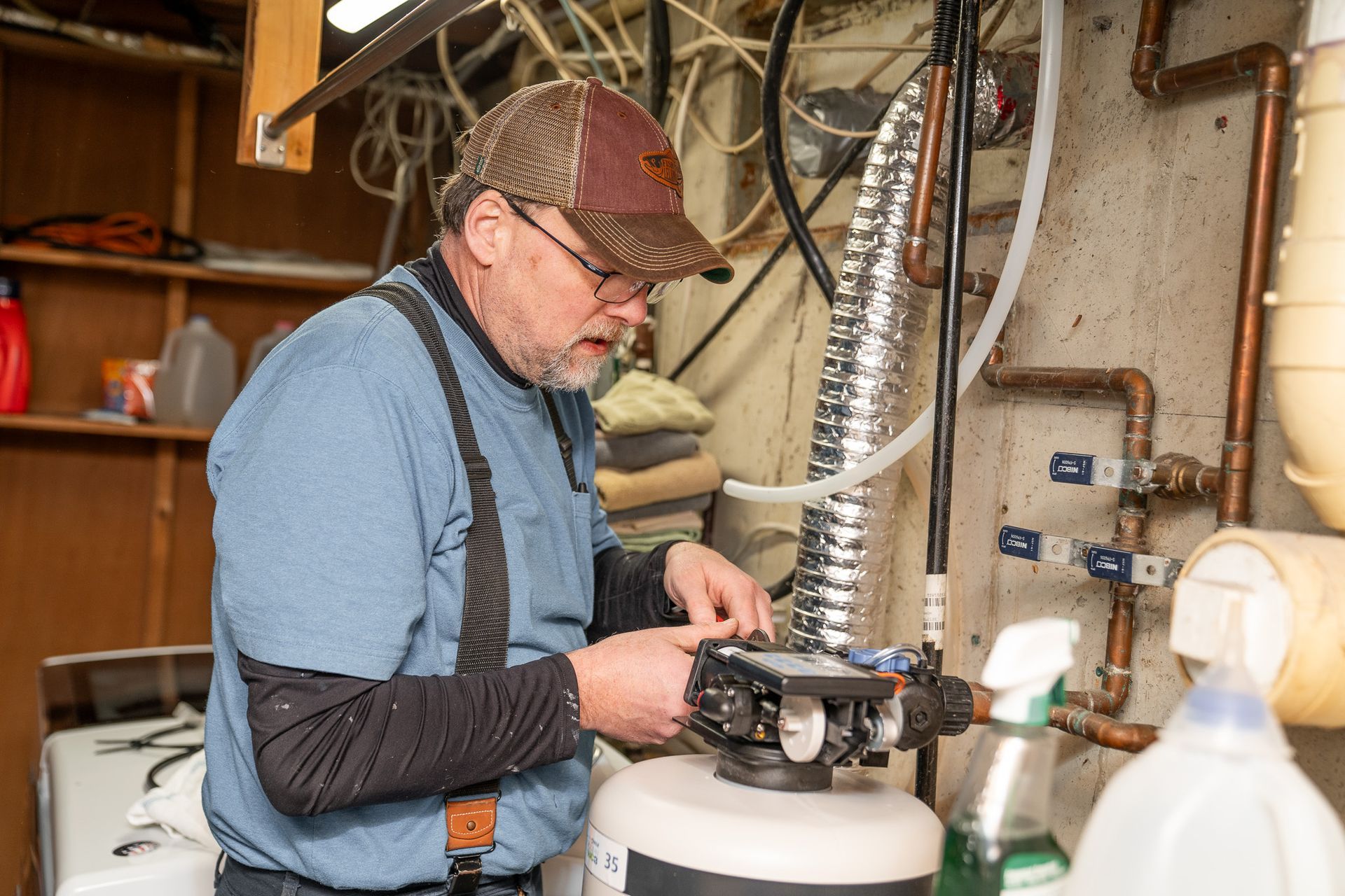 A man is working on a water heater in a basement.
