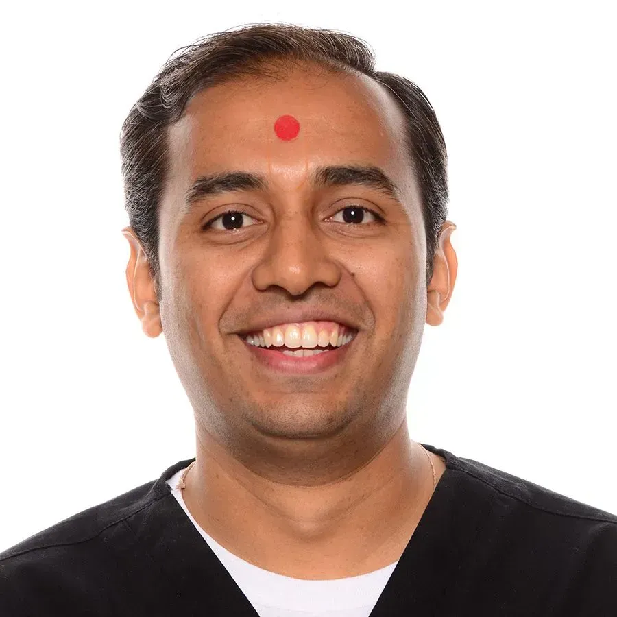 A man with a red dot on his forehead is smiling
