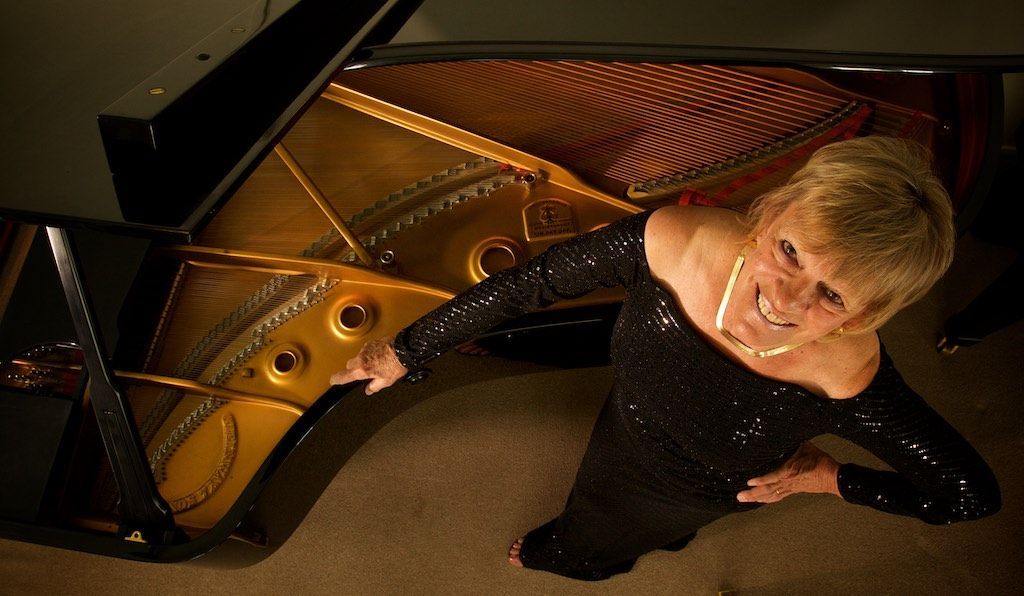 Jacquelyn Helin standing with her hand on a grand piano, phot is looking down vertically on her and the open piano.