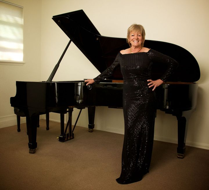 Jacquelyn Helin standing in front of a grand piano with her hand resting on the piano.