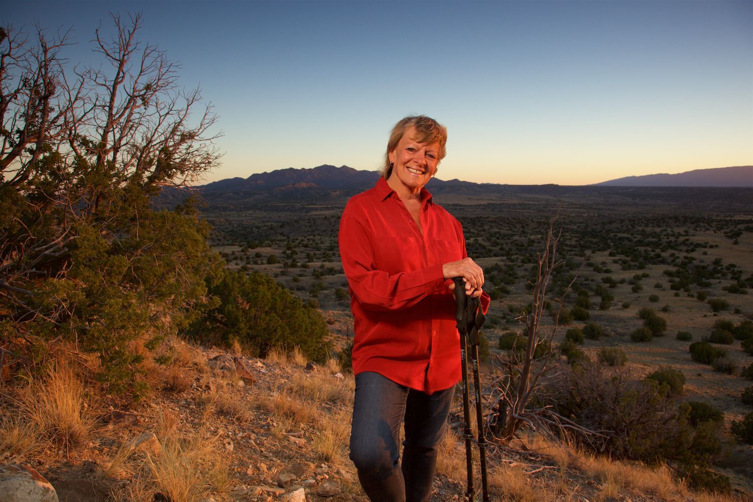 Jacquelyn Helin posing for a picture while on a hike in the desert of Santa Fe, New Mexico. She is resting on walking poles.