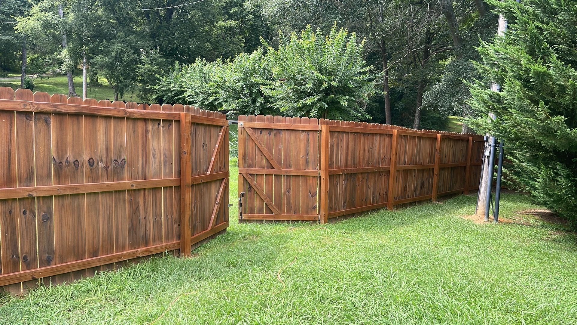 Wooden fence, brown stain, spanning across green grass in a backyard with trees.