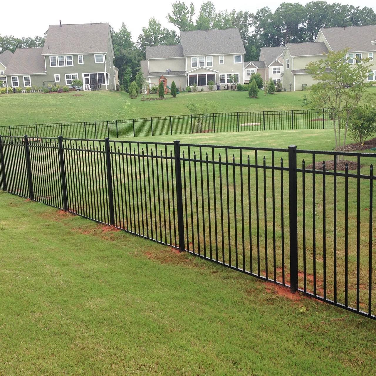 Black metal fence in a grassy yard, with houses on a hillside in the background.