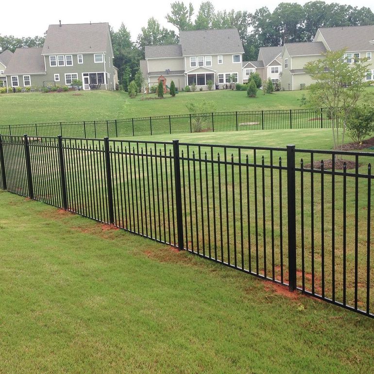 Black metal fence in a grassy yard, with houses on a hillside in the background.