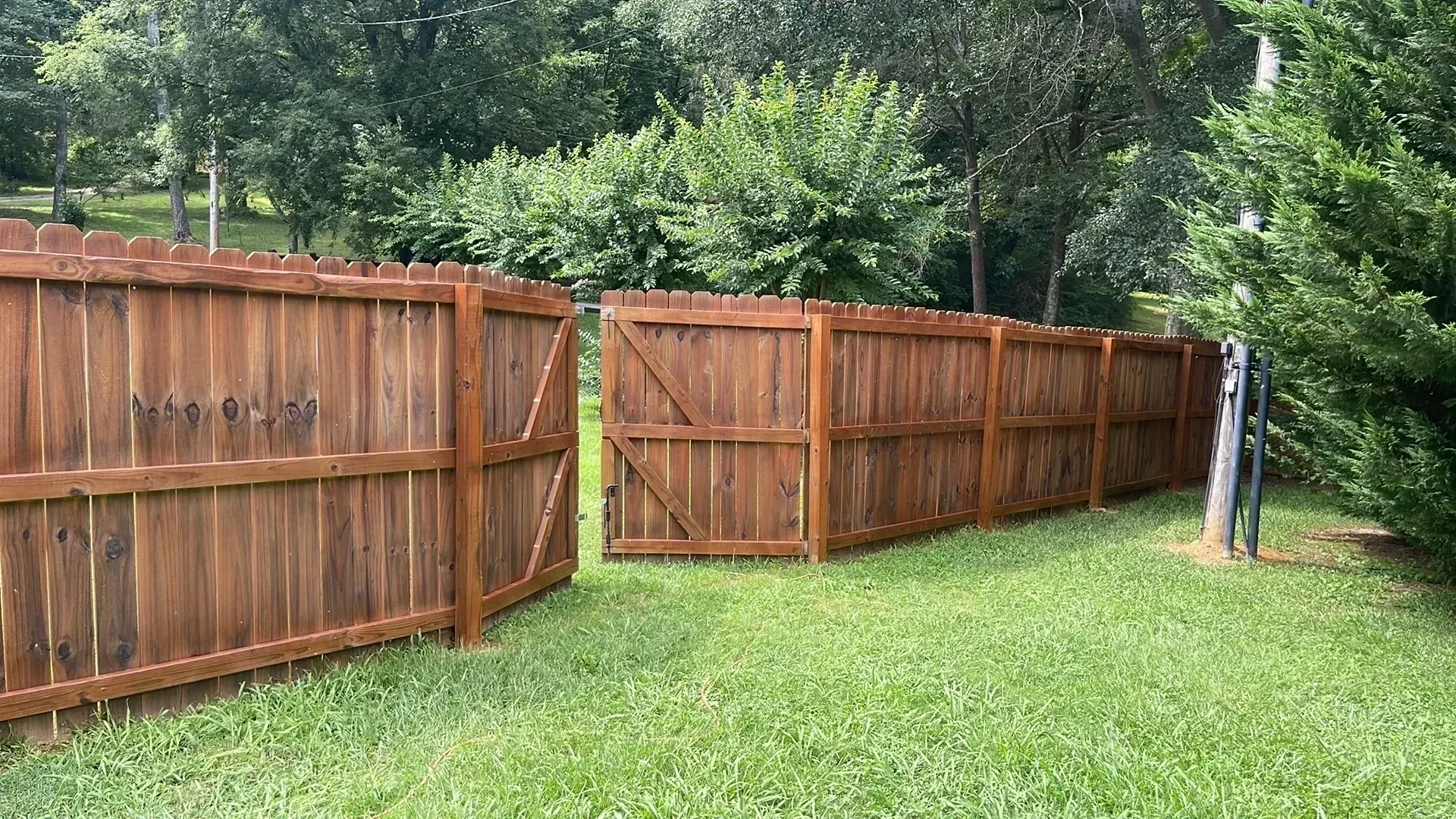 Brown wooden fence in a grassy yard, trees in background.
