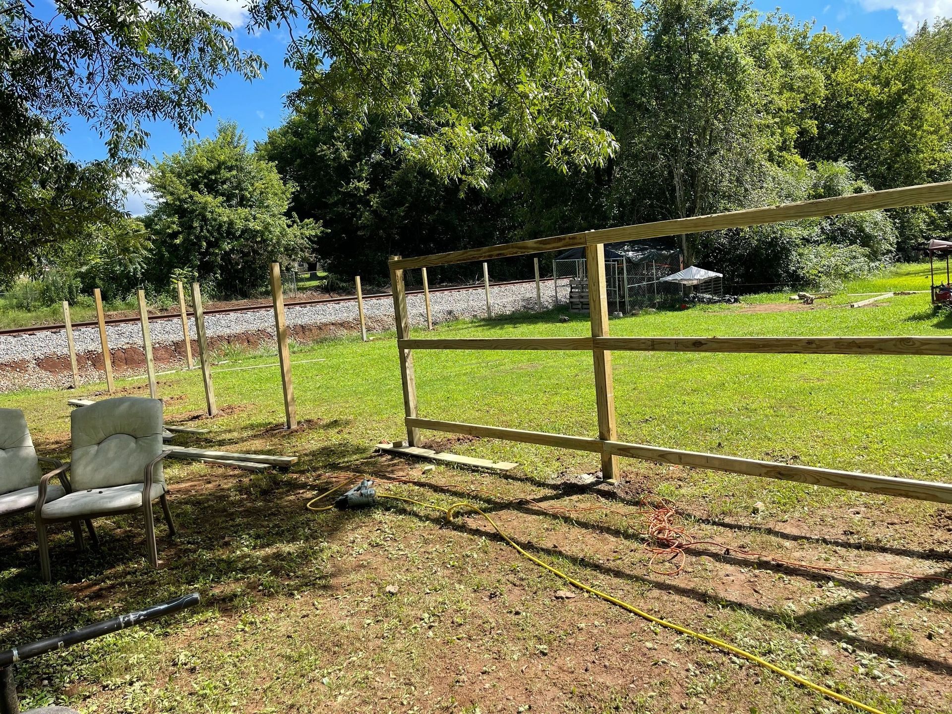 Wooden fence in a grassy yard, railway in the background, sunny day.
