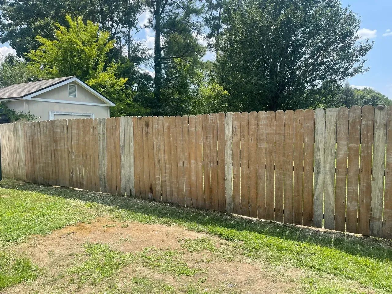 Wooden fence in a backyard with green grass, under a blue sky.