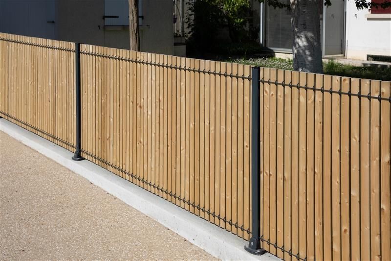 Wooden fence with vertical planks, black metal posts and horizontal bars, outside a house.