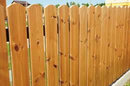 Wooden picket fence, stained light brown, outdoors, sunny day.