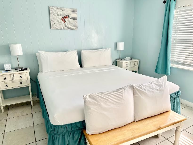 A bedroom with a bed , nightstands , lamps and a bench.
