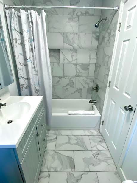 A bathroom with a bathtub , sink , mirror and shower curtain.