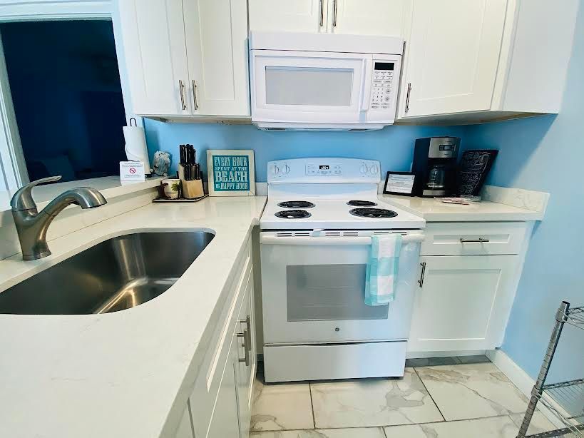 A kitchen with white cabinets , a white stove , a microwave and a sink.