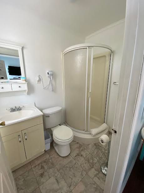 A bathroom with a toilet , sink , shower and mirror.