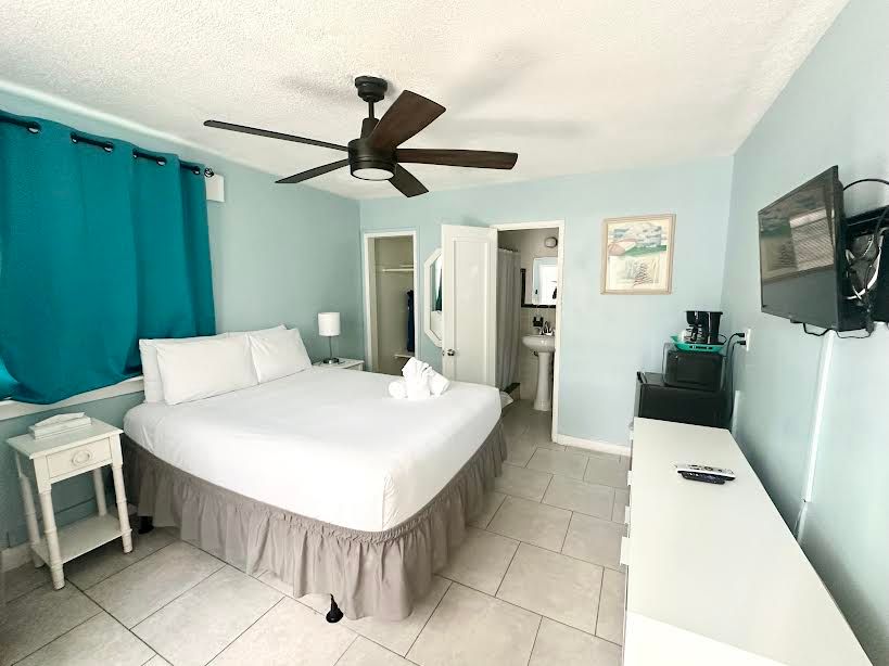 A hotel room with a king size bed , ceiling fan , television and nightstand.