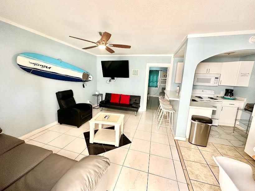 A living room with a surfboard hanging on the wall and a ceiling fan.