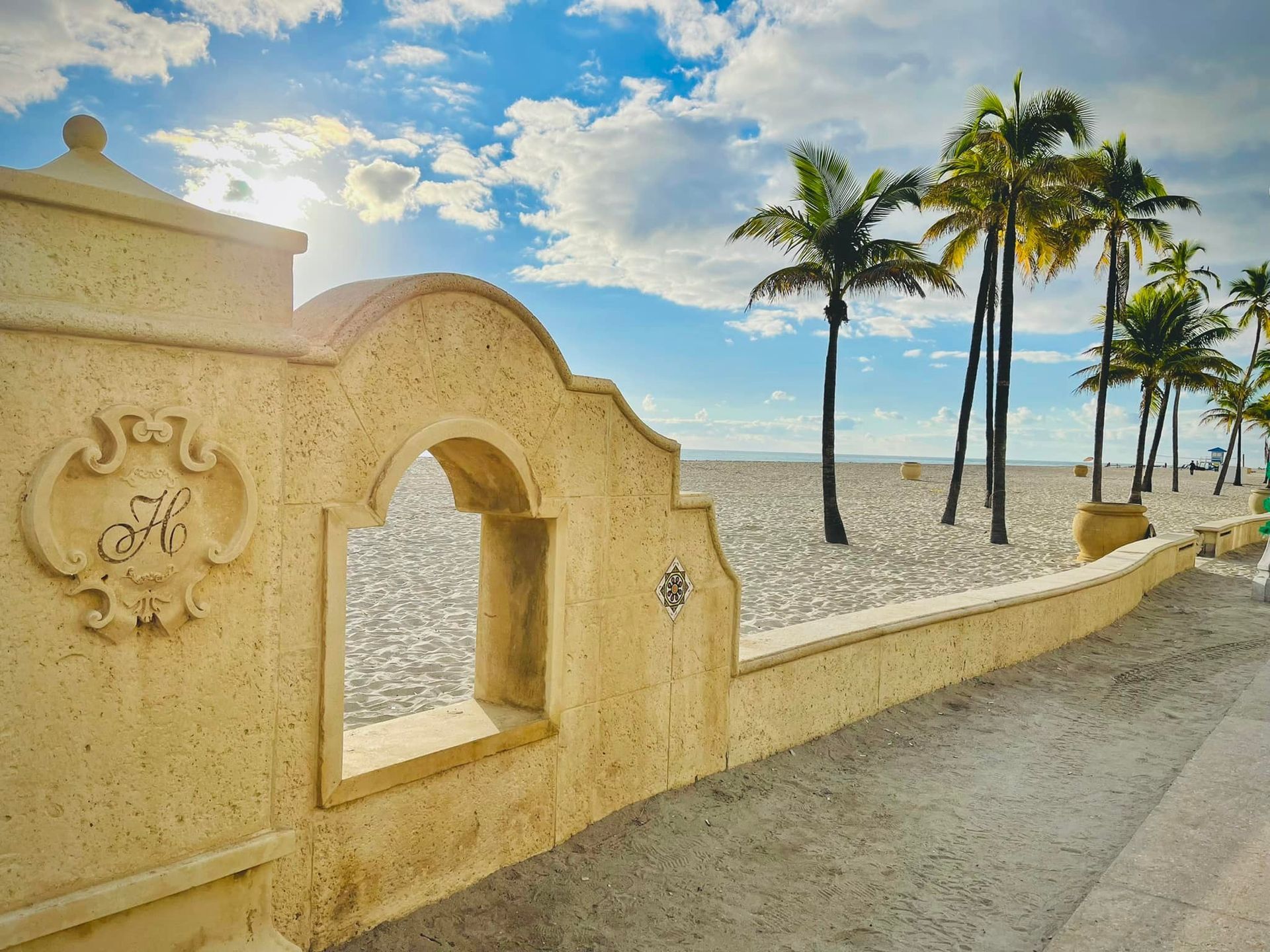 A stone wall leading to a beach with palm trees in the background.