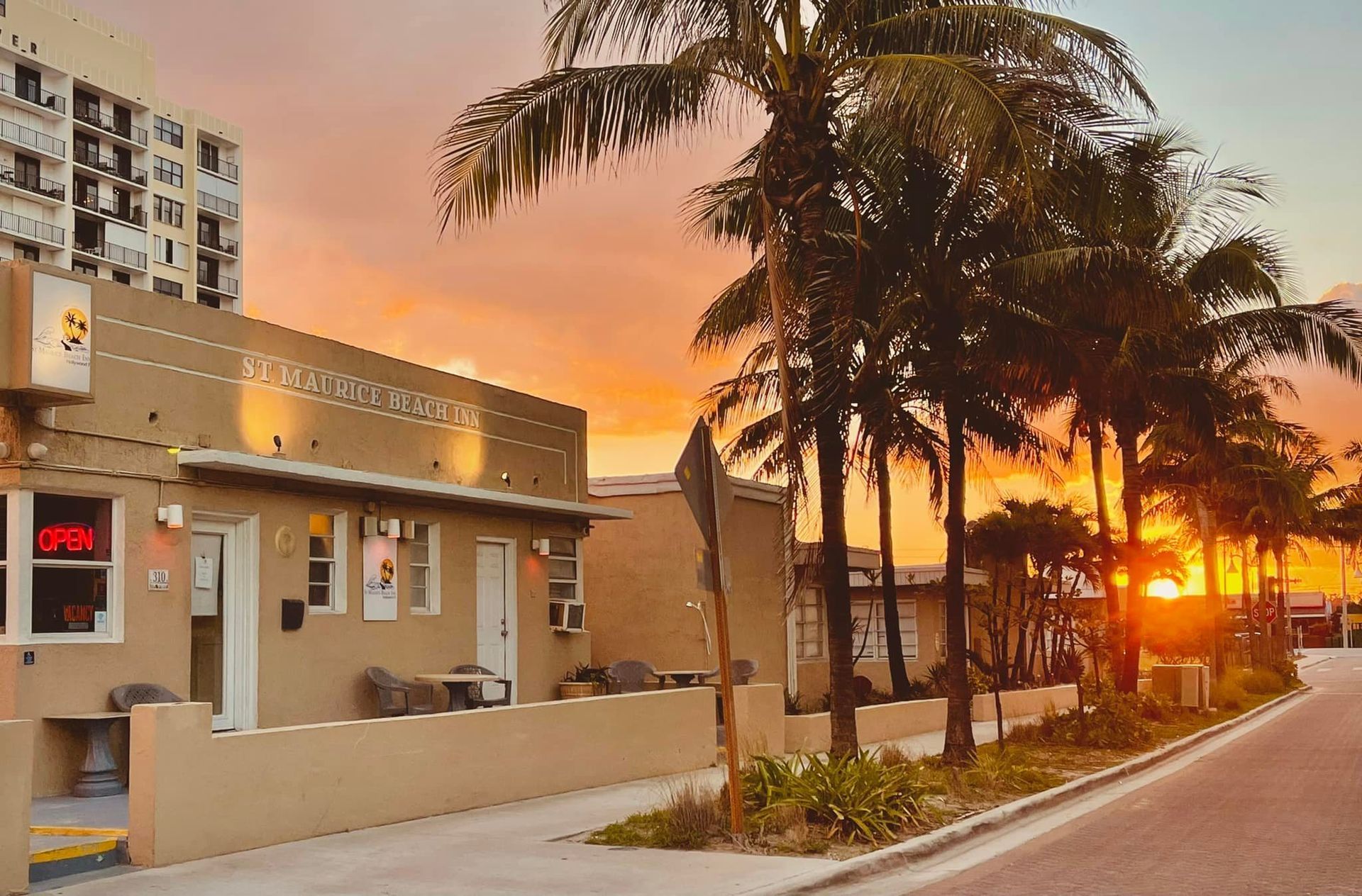 The sun is setting behind a building and palm trees.