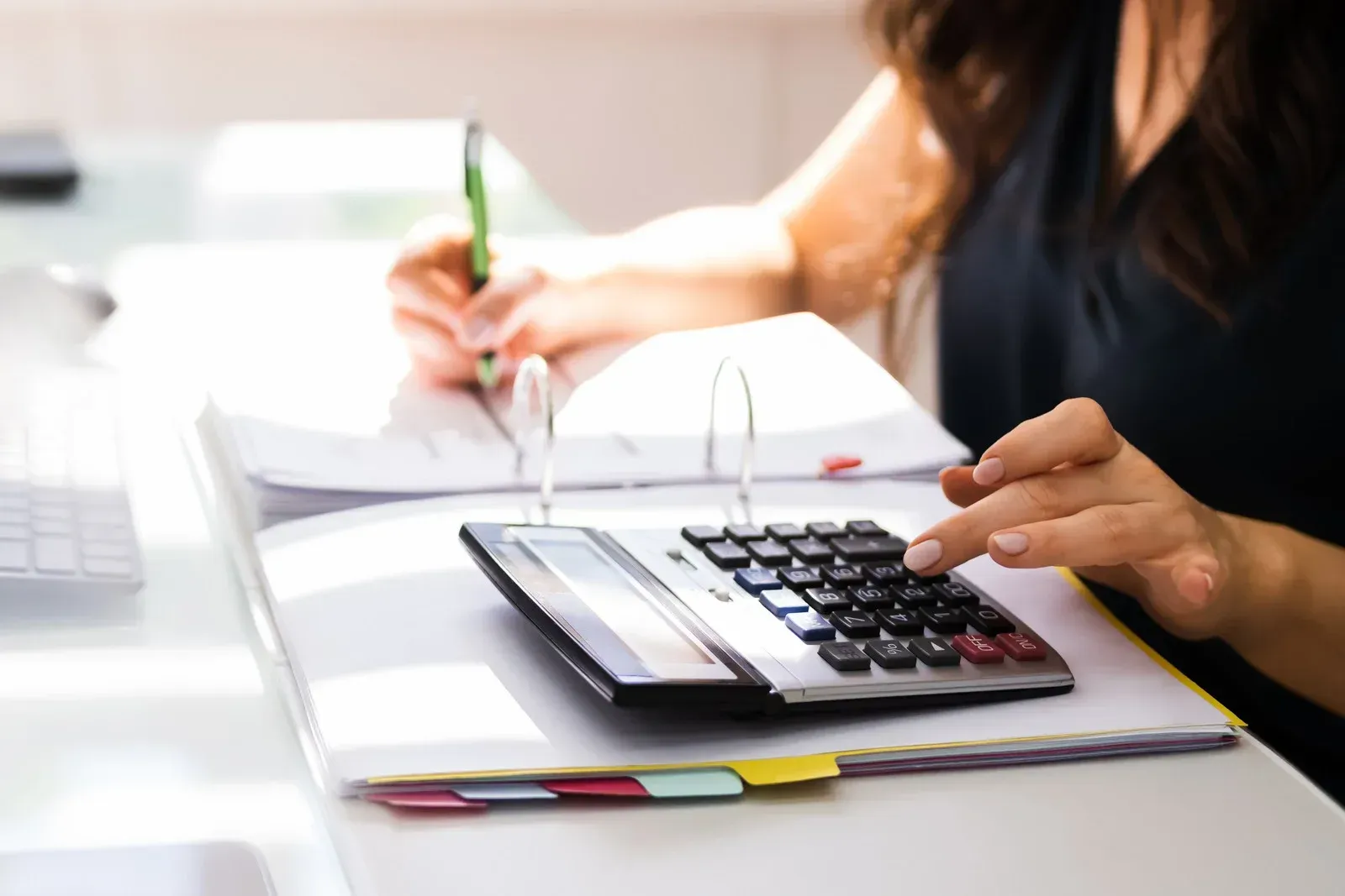 A woman is using a calculator while writing on a piece of paper.