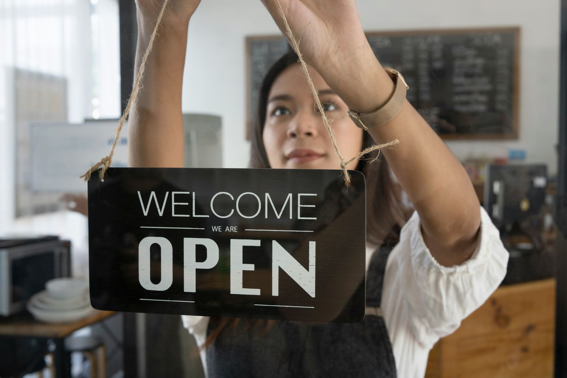A woman is hanging a welcome open sign in a restaurant.
