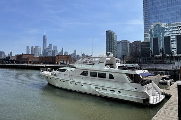 A large white yacht is docked in a harbor with a city skyline in the background.