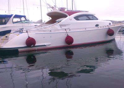 A white boat with red buoys on the side is docked in the water
