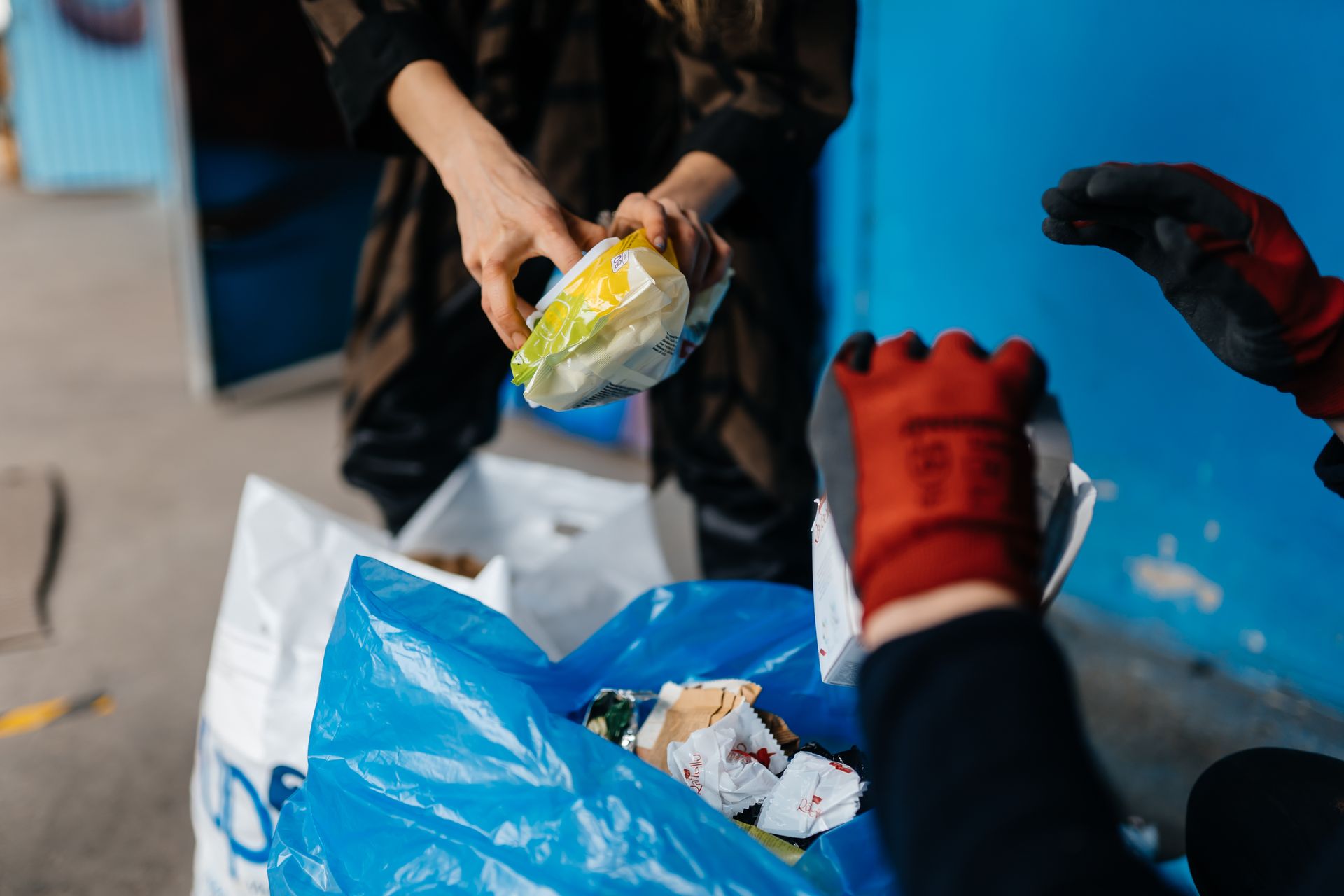 A person wearing red gloves is putting a bag of food into a blue bag