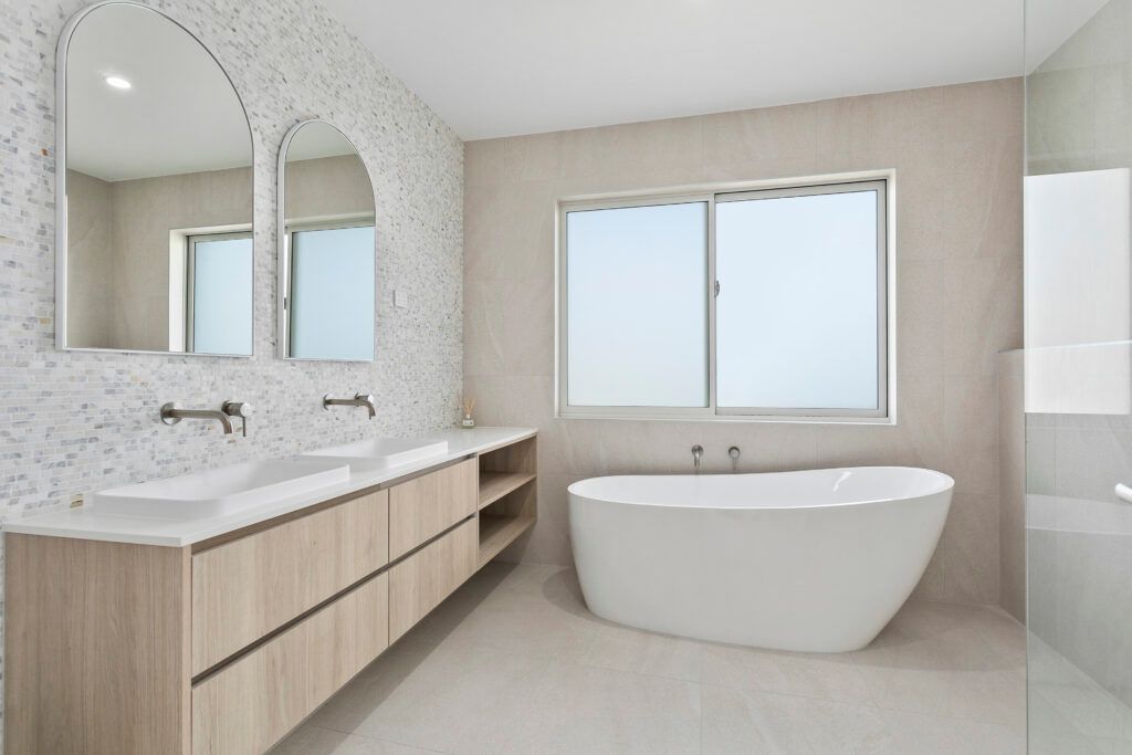 A Bathroom With a Bathtub, Sinks, Mirrors and a Window — Darko's Kitchens in Primbee, NSW
