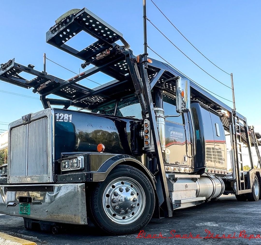 A glossy black semi-truck car hauler with chrome details parked outside under a clear blue sky.