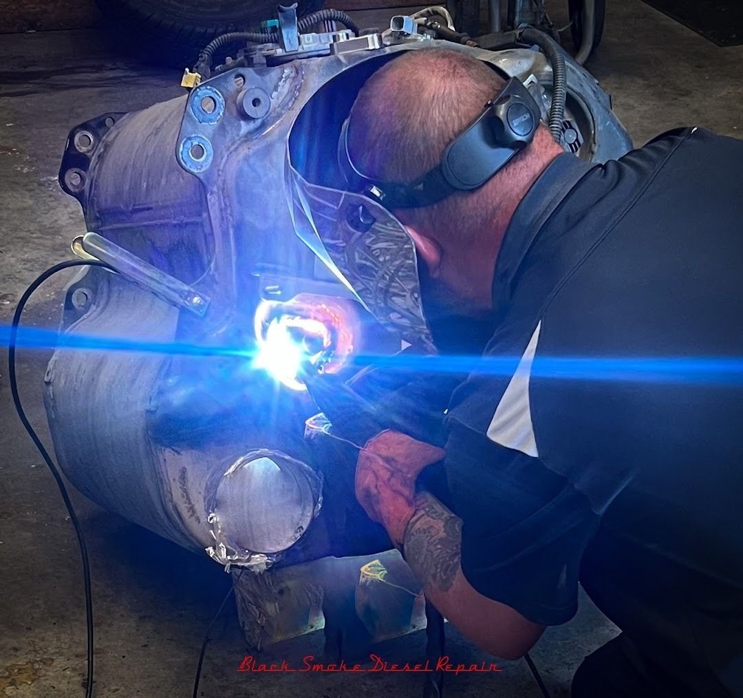 A person using a welding torch to repair a large metal automotive component in a workshop.