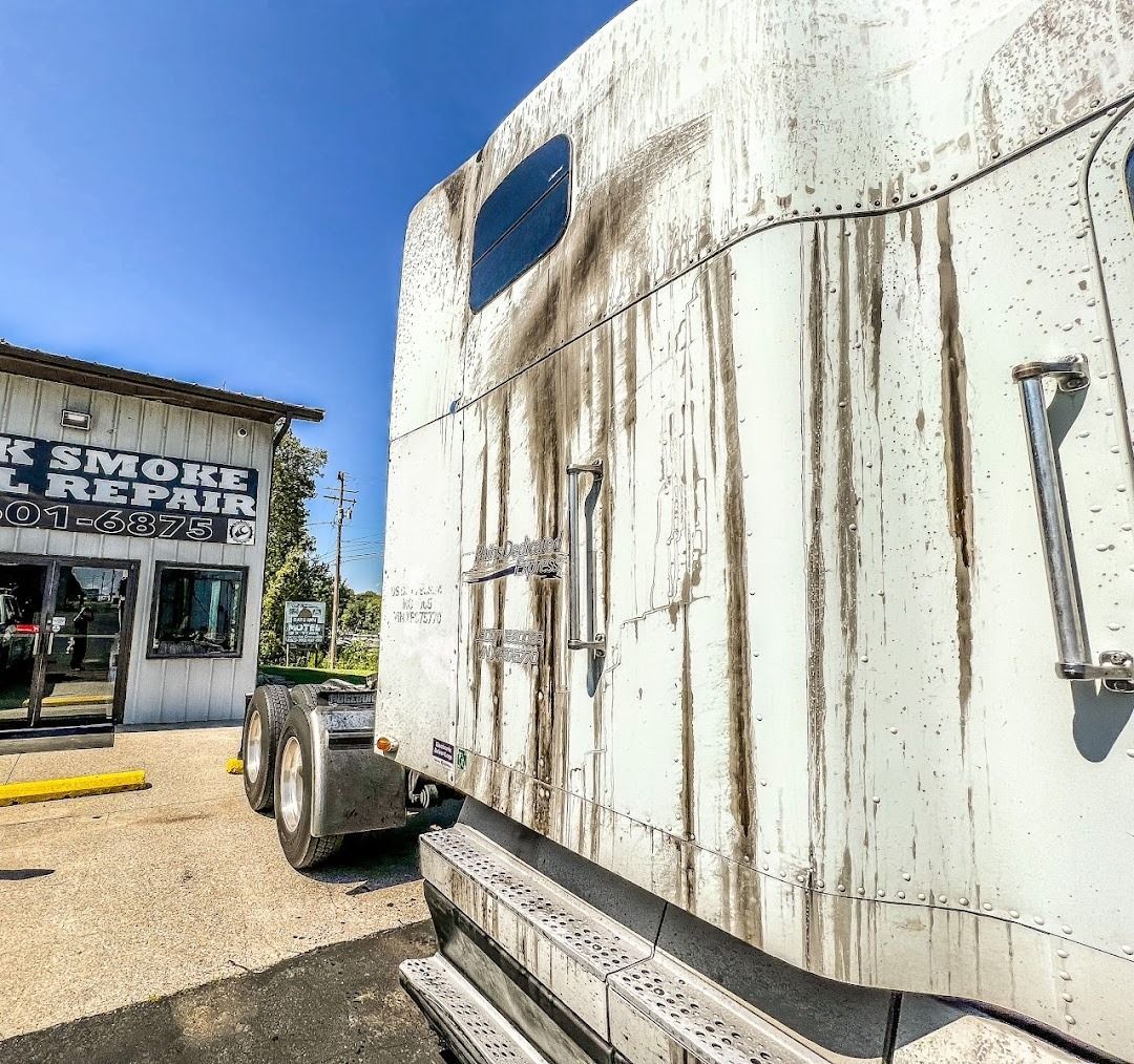 A dirty white semi-truck parked next to a building labeled 