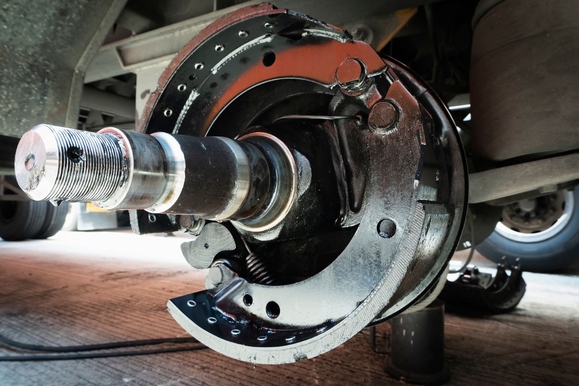 A close-up view of a car's metallic disc brake system with a silver brake caliper and suspension spring in a garage.