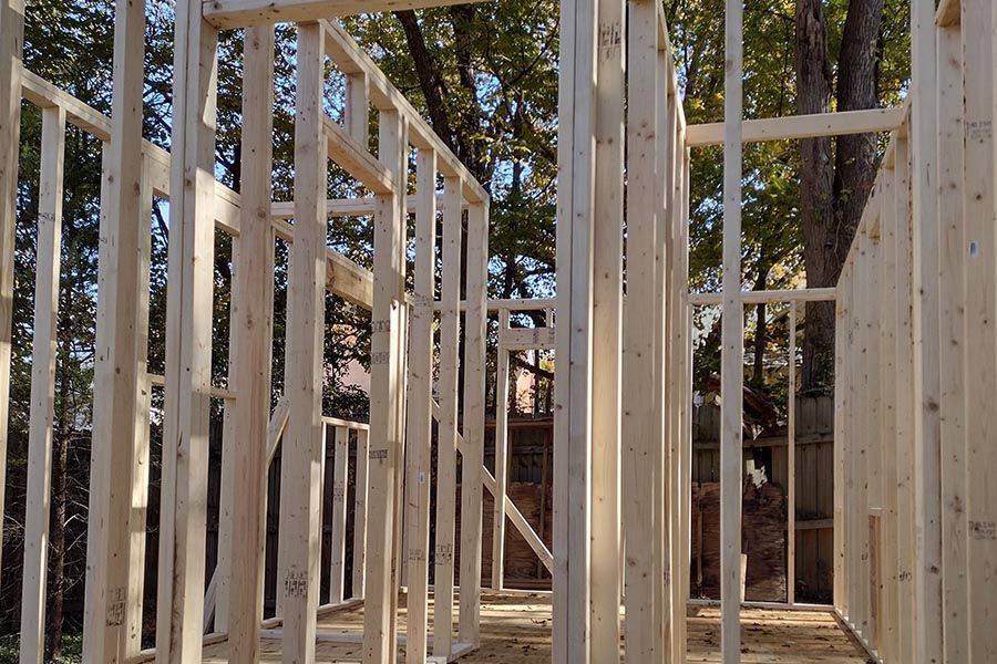 Wood-framed house under construction with exposed studs and trees in the background