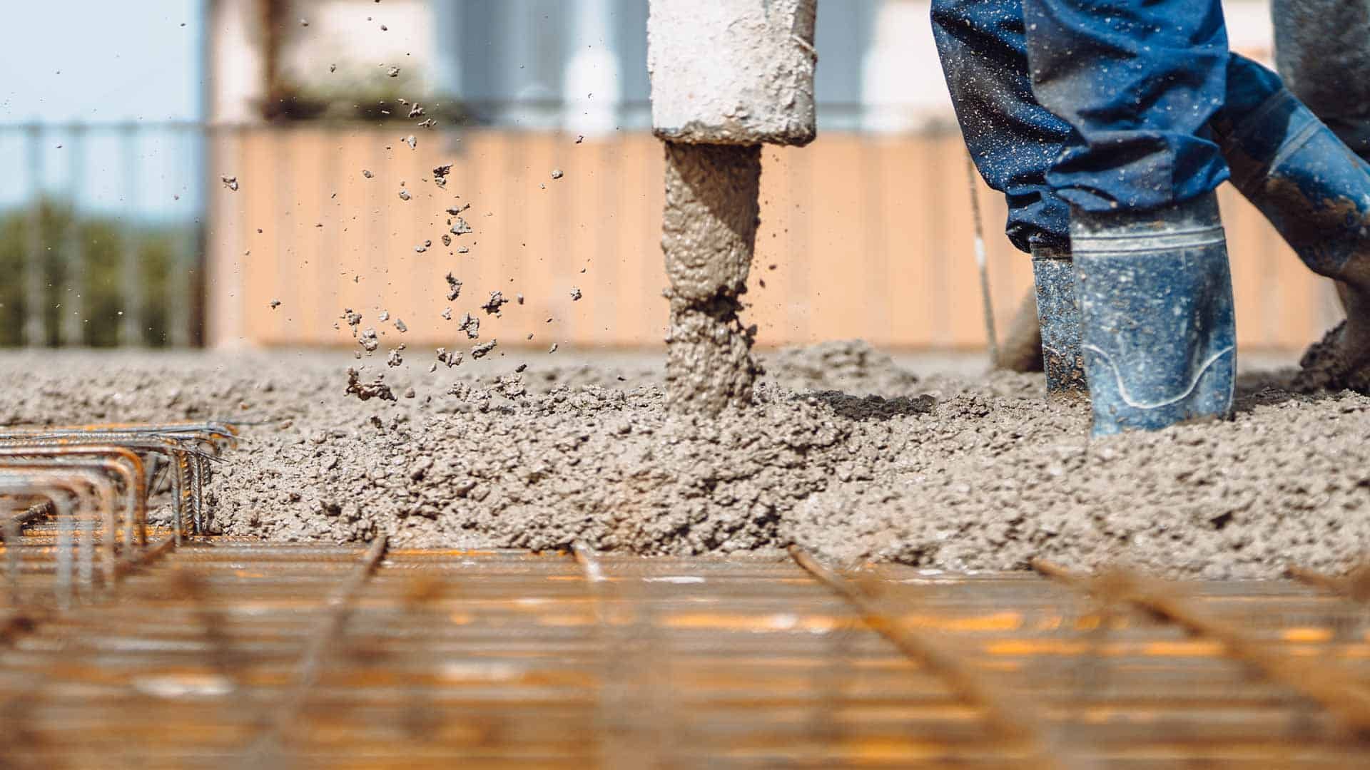 Concrete being poured onto rebar at a construction site, with a worker’s boot visible.