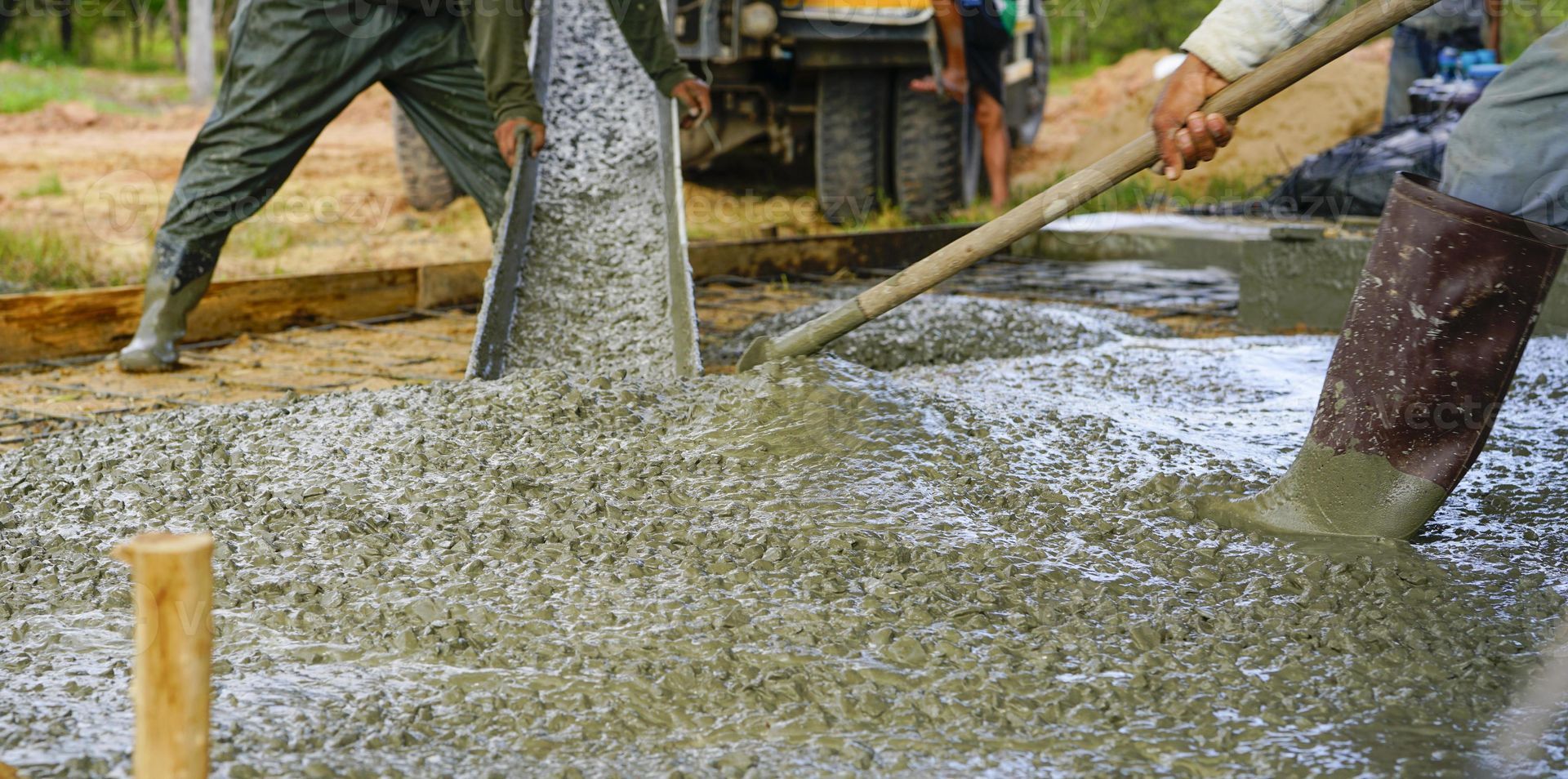 Workers mixing wet concrete with shovels at a construction site