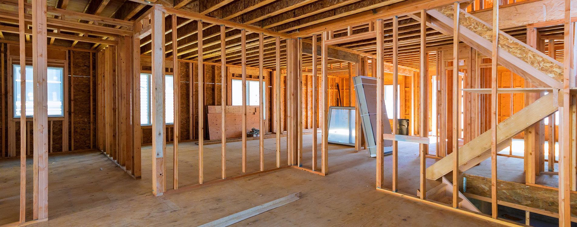 Exposed wooden framing inside a house under construction, with unfinished rooms and stairs visible.