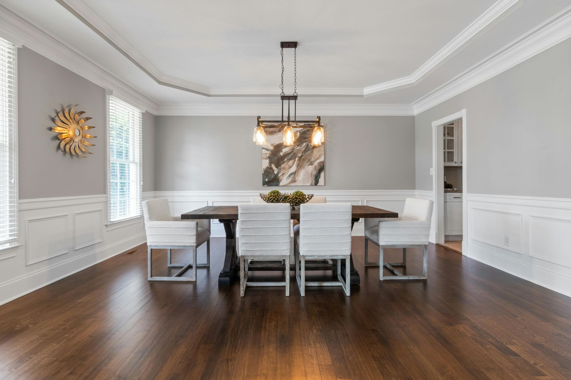 Bright dining room with white chairs, dark wood floors, and a pendant light over a long table.