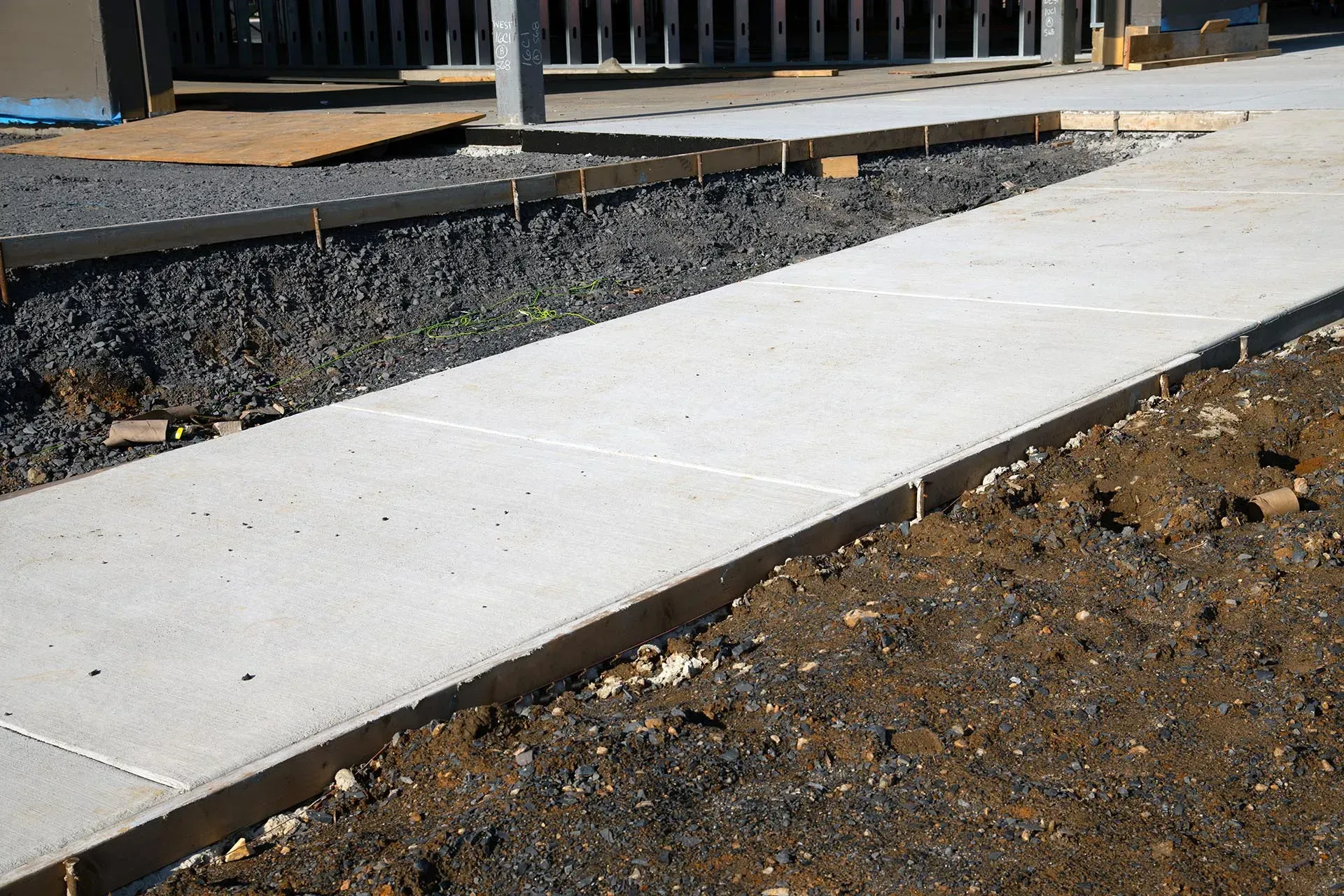 Concrete sidewalk beside a gravel yard and wooden deck railing.