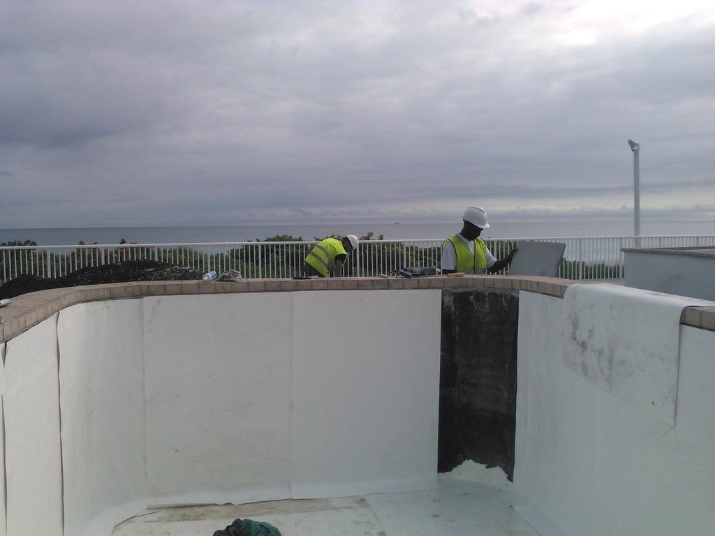 two men are working on a swimming pool with the ocean in the background .